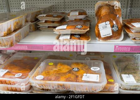 fresh halal chicken marinated in curry sauce on shelves for sale in an aisle at a Sainsburys supermarket, UK Stock Photo