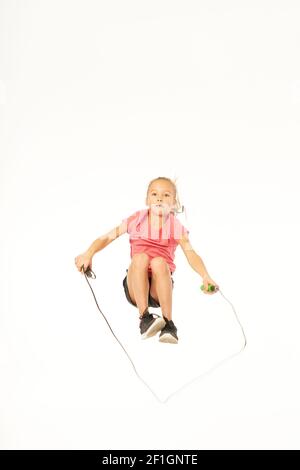 Cute female child in sportswear jumping and doing exercise with jump rope. Isolated on white background Stock Photo