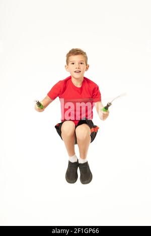 Cute male child looking at camera and smiling while holding jump rope and jumping. Isolated on white background Stock Photo