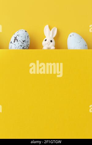A vertical shot of a cute bunny with easter eggs on yellow background with copy space Stock Photo