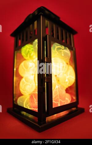 Close up of Easter egg shaped lights in a black lantern, on red background. Easter decoration concept. Fun and colorful Easter celebration concept. Stock Photo