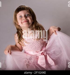Smiling blonde little girl with pink dress on grey and black and white background photoshoot in studio. Stock Photo
