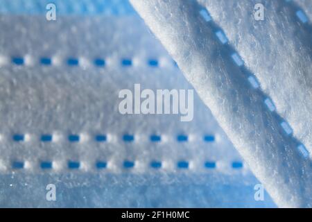 Disposable 3-ply face mask in blue color abstract background. Focus on foreground with plenty of copy space. Micro detail of medical face covering. Stock Photo