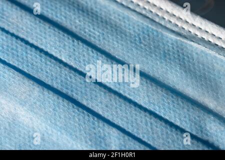 Close up of the front blue surface of a medical or surgical face mask. Man made single use item of Personal protective equipment, plastic texture. Stock Photo