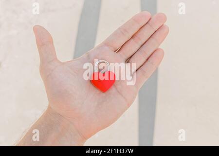 In the man's hand lies a small red heart in the form of a castle, a sign or symbol of love and romantic relationships. Stock Photo