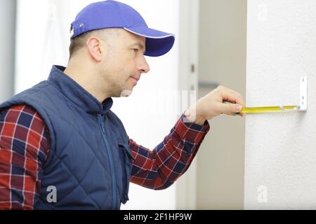 serious man using a measuring tape on white wall