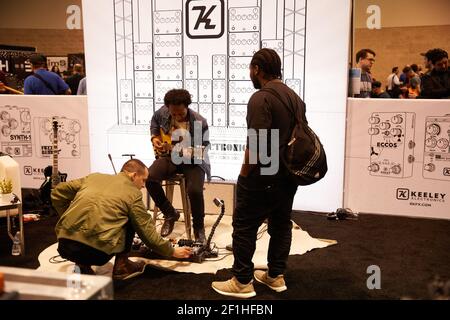 Black male electric guitar player sitting on stool playing Keeley guitar pedals at Musical Instrument Convention Stock Photo