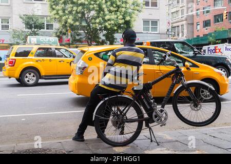 Delivery Man Leaning On His Bicycle Watching Taxis Pass By On Sixtth Avenue Stock Photo