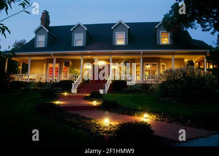 Cape cod style house lit for evening guest arriving for party by well lit walkways and welcoming views, Missouri Stock Photo