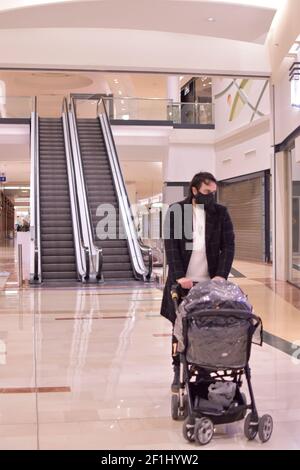 Man walking in empty mall. Single dad taking a walk with a stroller. Young man with his baby. Date: March first 2021. Stairs as background. Stock Photo