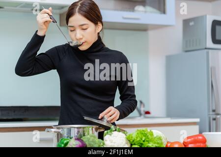 the woman is tasting the soup she cooks Stock Photo