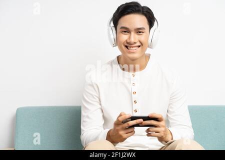 Asian man wearing wireless headphones and playing games on his phone Stock Photo