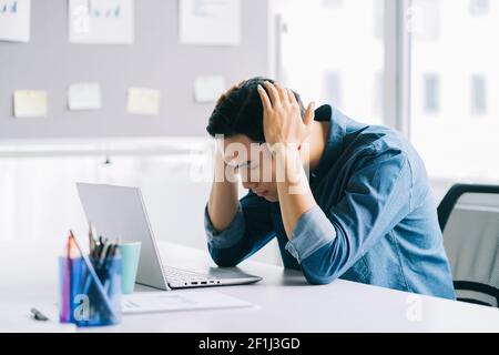 The Asian man is holding his head tired of having to work too much Stock Photo