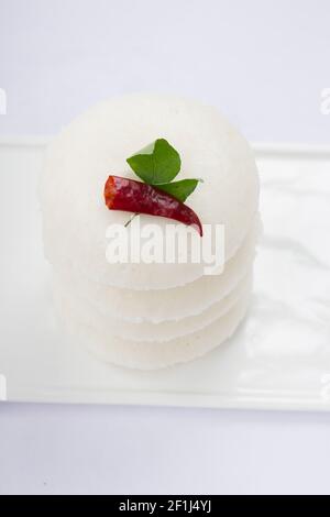 Idly or Idli, south indian main breakfast item garnished with red dry chilli and curry leaves  which is beautifully arranged on white rectangle base Stock Photo