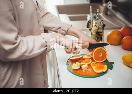 Close up photo of a caucasian woman slicing fruits in the kitchen and preparing a mojito Stock Photo