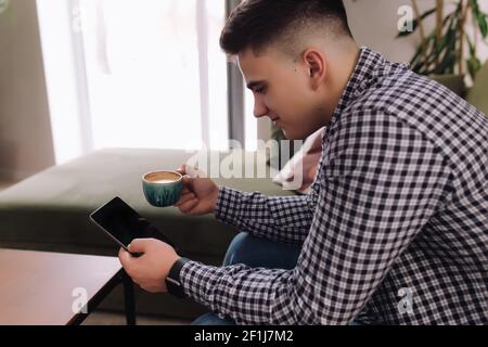 Smiling man holds and reading smartphone with black screen and coffee cup. Blurred background. High quality photo Stock Photo