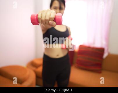Asian woman training to lift pink dumbbells for building muscle, concept of staying healthy by weight loss and recreation at their own residence. Stock Photo