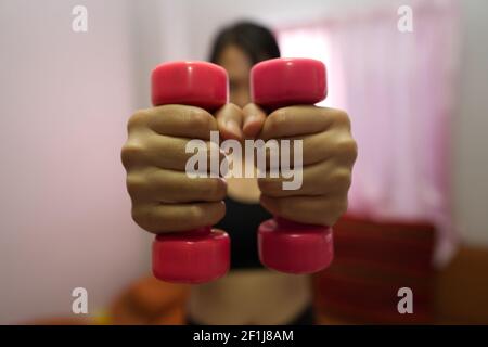 Asian woman training to lift pink dumbbells for building muscle, concept of staying healthy by weight loss and recreation at their own residence. Stock Photo