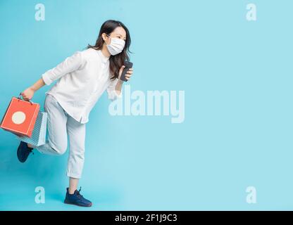Beautiful Asian woman wearing white mask carrying shopping bag and phone in hand while running Stock Photo