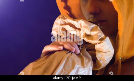 Teenage girl in orange hooded sweatshirt drinks a super alcoholic bottle wrapped in a paper bag Stock Photo