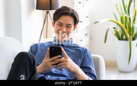 Young Asian man lying on sofa and using phone Stock Photo