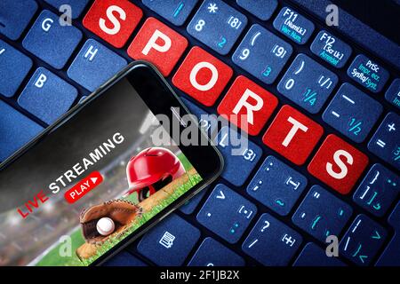 Sports Live streaming concept showing baseball game broadcast on smartphone with laptop high tech background. Accessible on demand digital content is Stock Photo