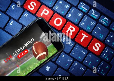 Sports Live streaming concept showing Football game broadcast on smartphone with laptop high tech background. Accessible on demand digital content is Stock Photo