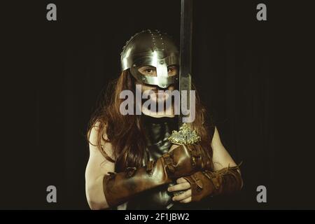 Viking warrior with metallic helmet and animal skins. leather gauntlets, red wooden shield with gold decorations and steel sword Stock Photo