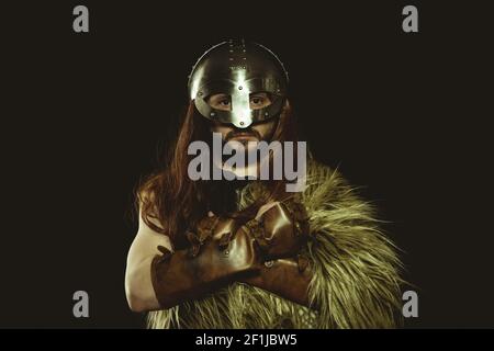 Viking warrior with metallic helmet and animal skins. leather gauntlets, red wooden shield with gold decorations and steel sword Stock Photo