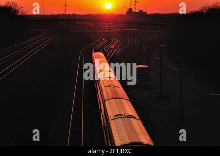 The setting sun reflecting off a Metra commuter train leaving Aurora, Illinois bound for Chicago. Stock Photo
