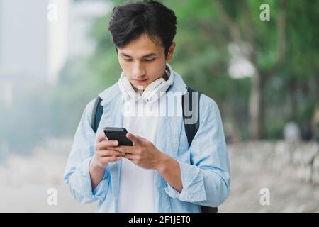 Young Asian man wearing backpack and looking at phone screen Stock Photo
