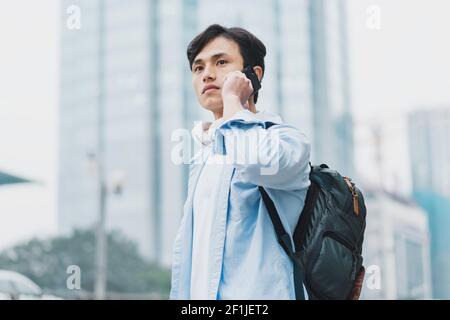 young asian man wearing a backpack and is on the phone Stock Photo