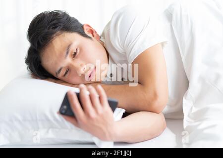Young man lying in bed using a phone Stock Photo