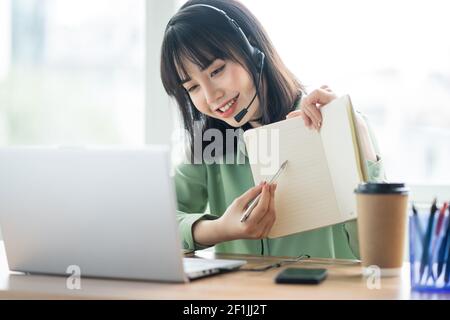 Beautiful asian customer service lady is calling customers to offer products Stock Photo