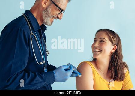 Smiling woman looking at doctor while receiving vaccine. Friendly doctor giving vaccine to young woman. Stock Photo