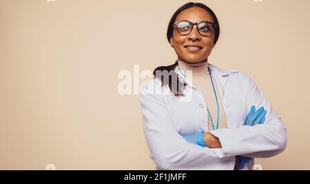 African woman healthcare professional looking away on brown background. Female doctor with her arms crossed. Stock Photo