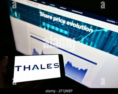 Person holding mobile phone with business logo of French defence company Thales S.A. on screen in front of website. Focus on phone display. Stock Photo