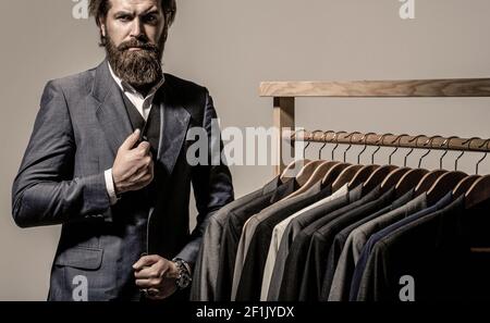 Male suits hanging in a row. Men clothing, boutiques. Tailor, tailoring. Stylish men's suit. Man suit, tailor in his workshop. Handsome bearded Stock Photo