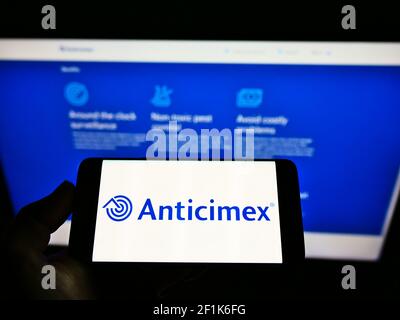 Person holding mobile phone with business logo of Swedish pest control company Anticimex AB on screen in front of web page. Focus on phone display. Stock Photo