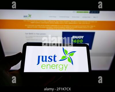 Person holding cellphone with business logo of Canadian power company Just Energy Group Inc. on screen in front of webpage. Focus on phone display. Stock Photo