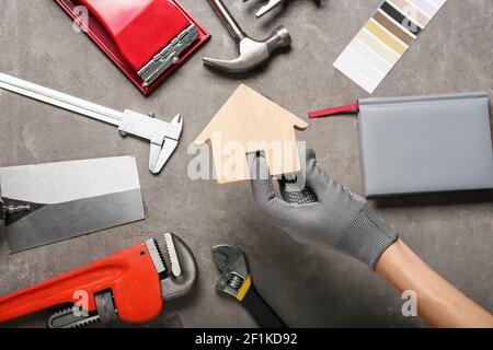 Female hand with figure of house and construction tools on grunge background Stock Photo