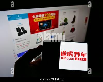 Person holding mobile phone with logo of Chinese automotive parts company Tuhu on screen in front of website with web shop. Focus on phone display. Stock Photo