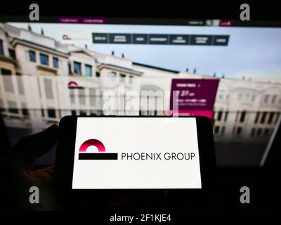 Person holding smartphone with logo of British insurance company Phoenix Group Holdings plc on screen in front of website. Focus on phone display. Stock Photo