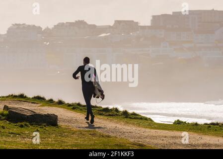 A male surfer carrying his surfboard and running along the coast path towards Fistral in Newquay in Cornwall. Stock Photo