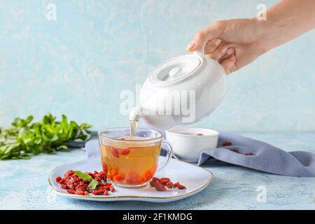 Woman pouring goji tea from teapot into cup  on color background Stock Photo