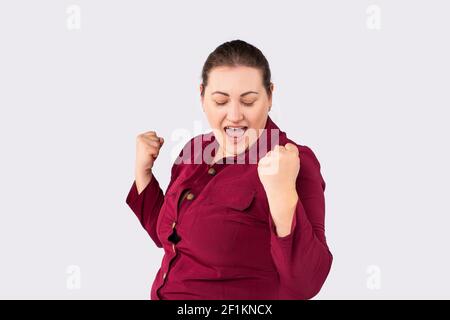 Happy plus size woman celebrating and dancing for female power. Curvy overweight lady having fun on gray background. Emancipation and confident Stock Photo