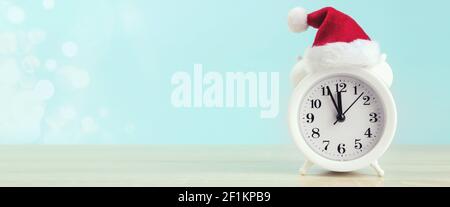 Close-Up Of Alarm with red santa cup On Table Against Blue Wall, banner format Stock Photo