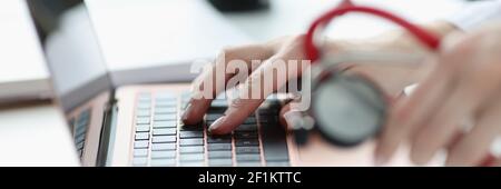 Doctors hands holding stethoscope and typing on keyboard closeup Stock Photo