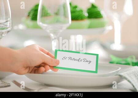 Woman putting card with text "St. Patrick's Day" on plate Stock Photo