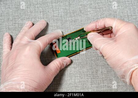 Worker hands with tweezers repairing the pcb with a small microchip. Manufacture work processes concept Stock Photo
